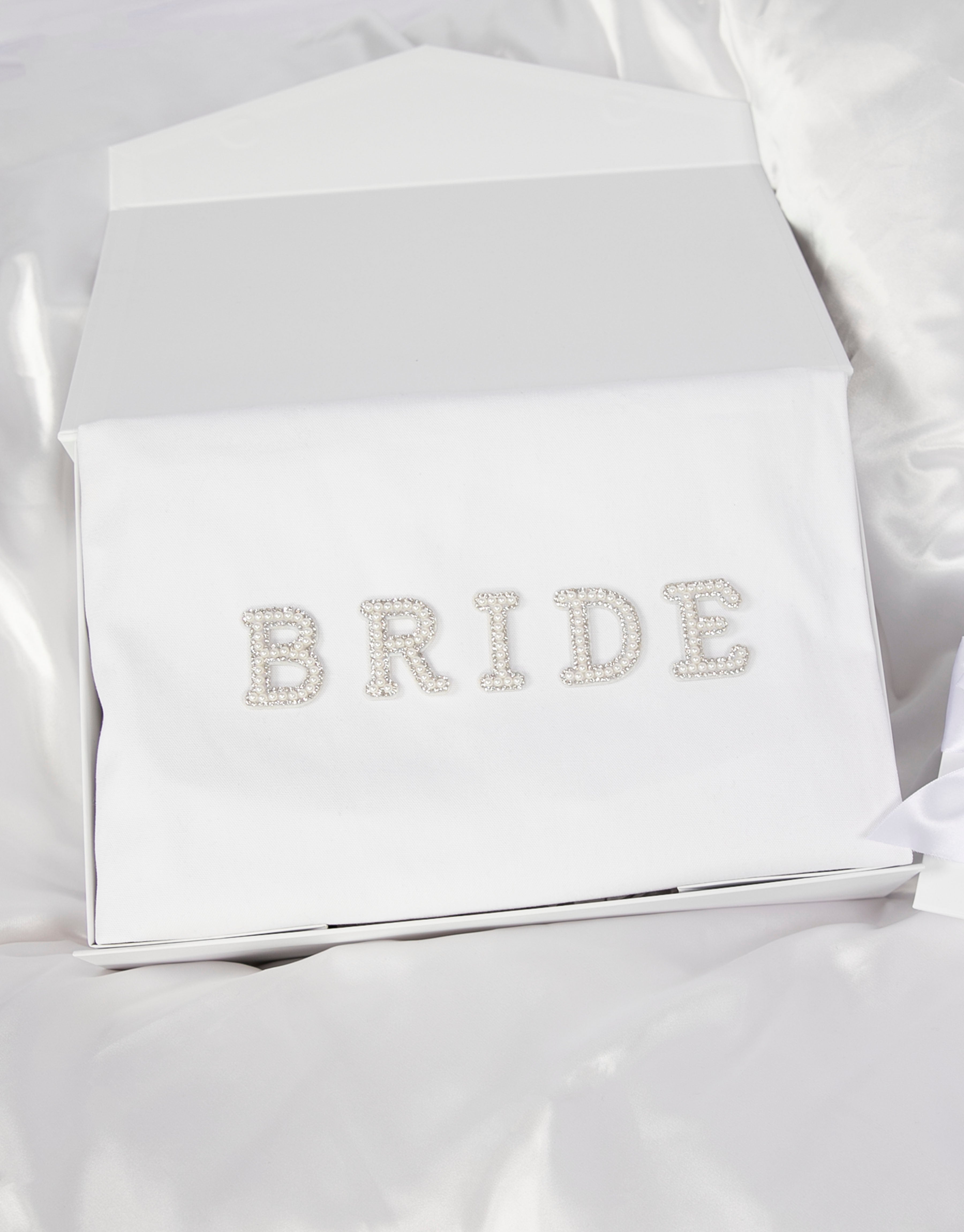 23Dreams Whitehaven Bliss Bridal Box: white tote bag with "bride" pearl and rhinestone patches, 2 petite white gift boxes; one Mini Love hearts Bath Bomb Fizzies; hamptons deluxe candle whitehaven sea salt; ultra soft satin sleep eye mask white; scrunchie soft silky satin white; luxe silky camisole set white; Elegant 18K Gold Plated Letter Pearl Necklace; glamour pearls hair pin set in gold 18 pins; white pearls gold hair pin set luxe glam and white pearled hair clip set in gold timeless elegance.