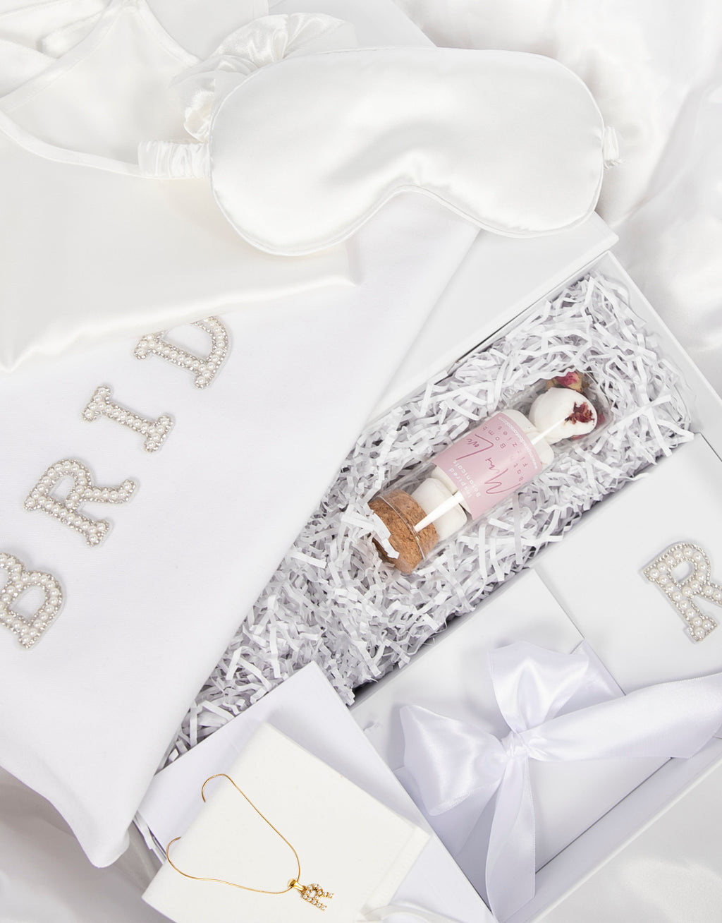 23Dreams Whitehaven Bliss Bridal Box: white tote bag with "bride" pearl and rhinestone patches, 2 petite white gift boxes; one Mini Love hearts Bath Bomb Fizzies; hamptons deluxe candle whitehaven sea salt; ultra soft satin sleep eye mask white; scrunchie soft silky satin white; luxe silky camisole set white; Elegant 18K Gold Plated Letter Pearl Necklace; glamour pearls hair pin set in gold 18 pins; white pearls gold hair pin set luxe glam and white pearled hair clip set in gold timeless elegance.
